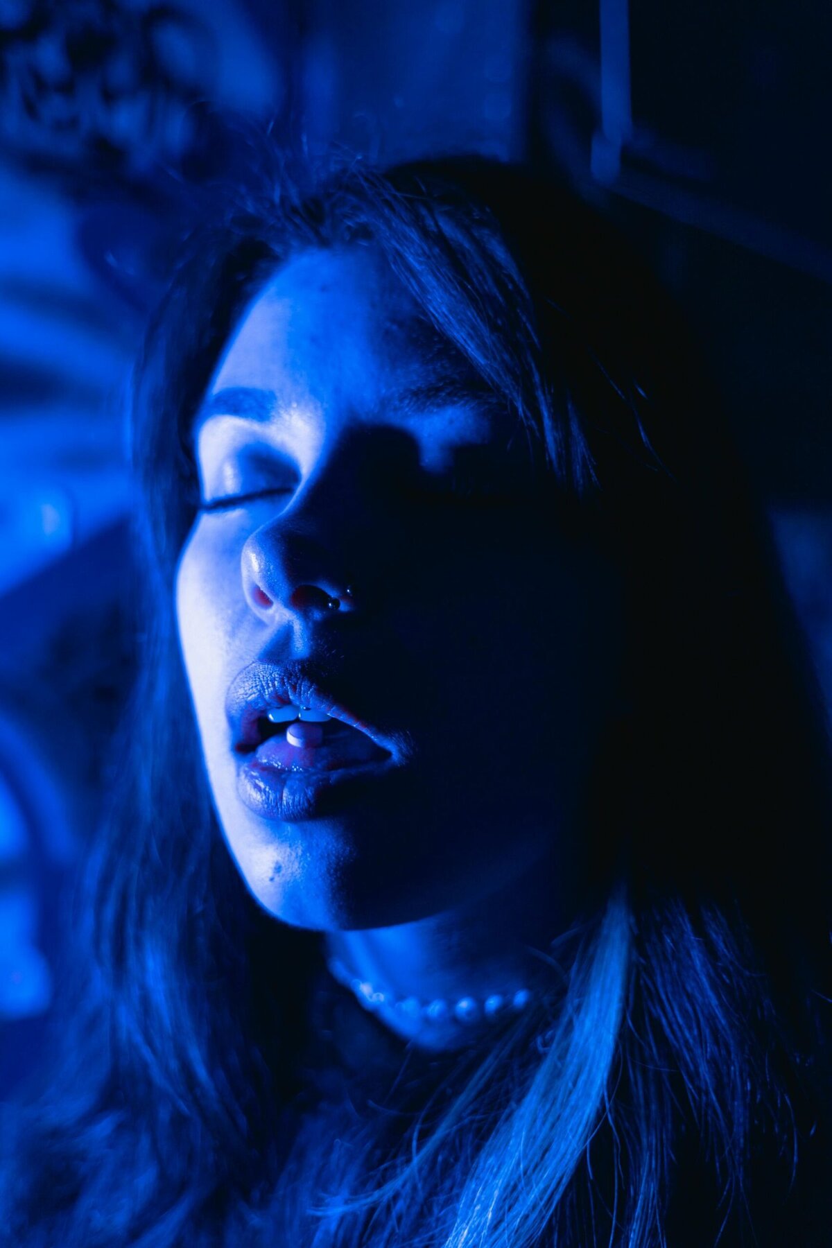 Serene woman with closed eyes illuminated by blue light, showcasing tranquility and inner peace.